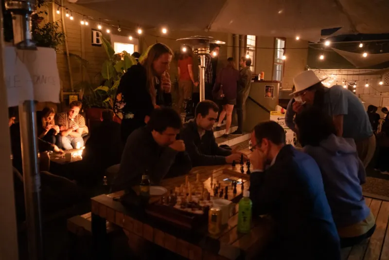 Attendees playing chess at night under string lights at Manifest