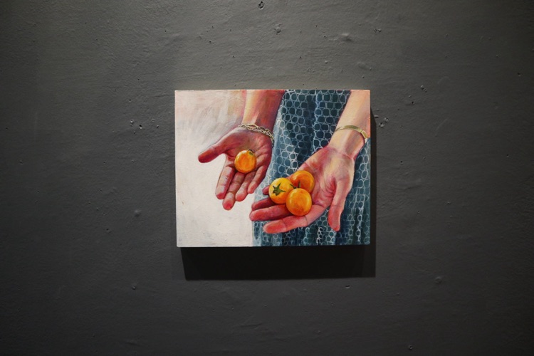 Painting of hands holding tomatoes hung in a gallery