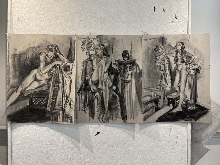 Three charcoal figure drawings taped to a wall